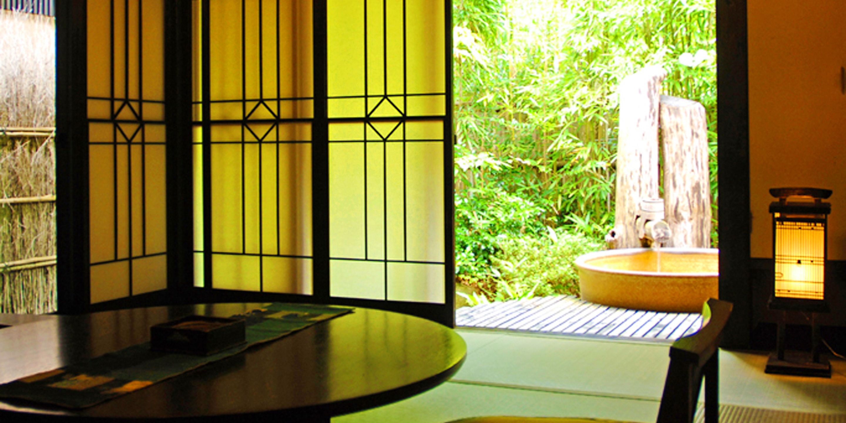 A traditional Japanese room with tatami flooring, a low table, a sliding door with a view of a bamboo garden, and a lantern.