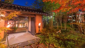 Uma casa tradicional japonesa com telhado de telhas, porta de madeira e caminho de pedra que leva à entrada.