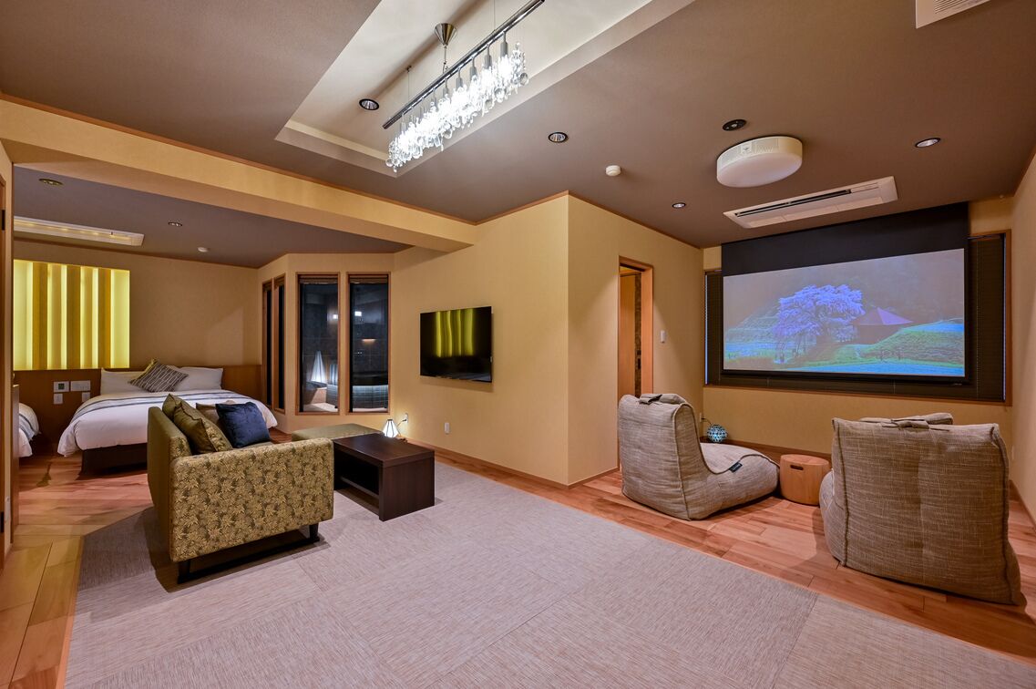 Quarto de hotel com cama, sofá, televisão e tela de projeção.