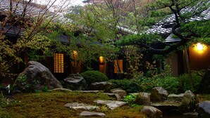 Um jardim japonês tradicional com formações rochosas, musgo e um edifício de madeira com telhados de telha.
