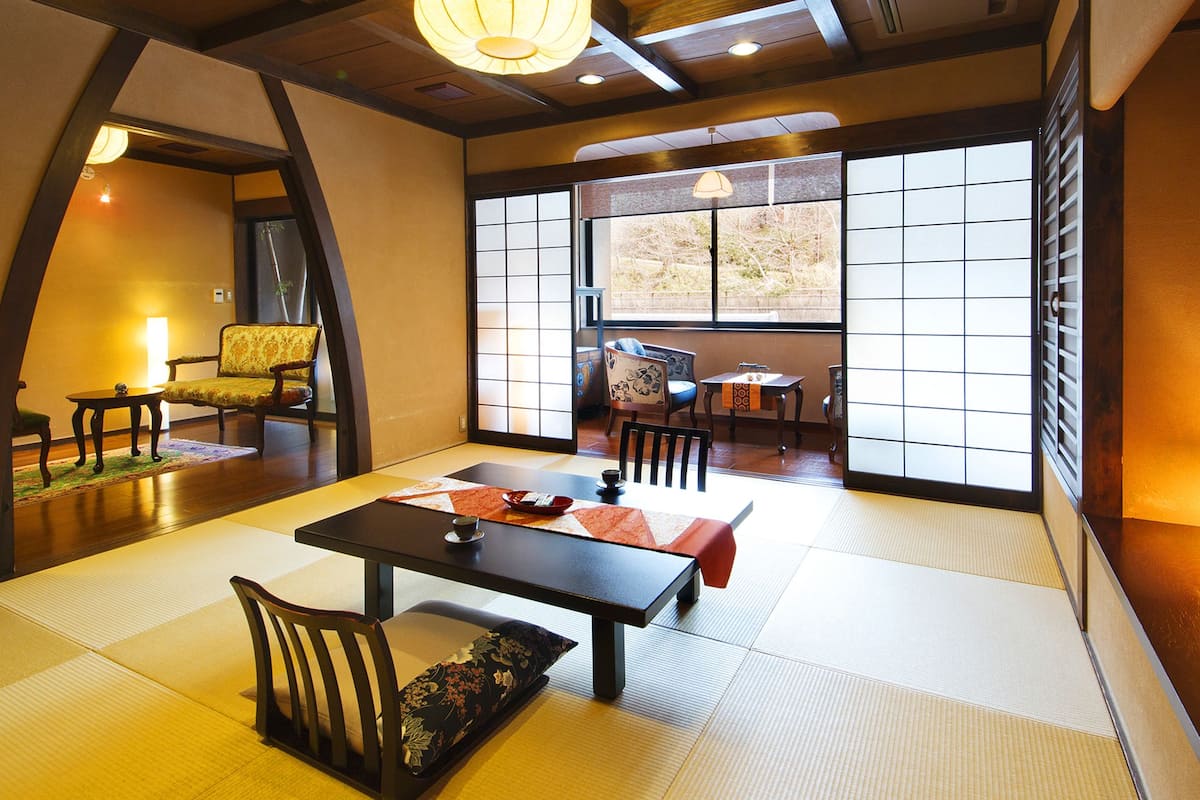 Une pièce de style japonais traditionnel, avec un sol recouvert de tatamis, une table basse et une vue à travers des panneaux coulissants en papier.
