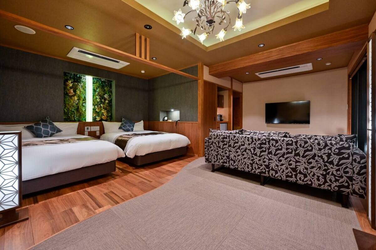 Une chambre d’hôtel moderne avec deux lits, un canapé, une télévision et un mur décoratif.