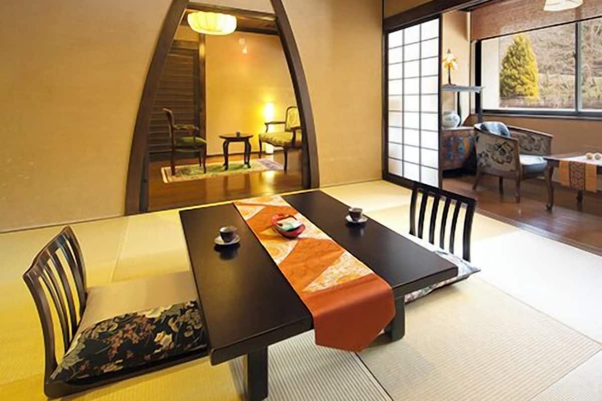 Une pièce de style japonais traditionnel, avec un sol recouvert de tatamis, une table basse et une vue sur l’extérieur.