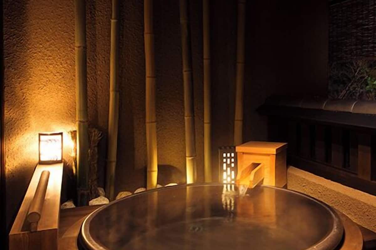 Un jacuzzi rond, doté d’un bord en bois, entouré de plantes de bambou et d’un mur de pierre.