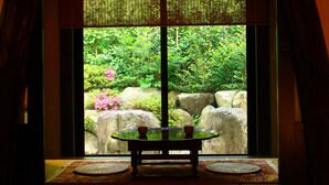Quarto com vista para um jardim através de uma janela, uma mesa com uma tigela e um tapete tecido no chão.
