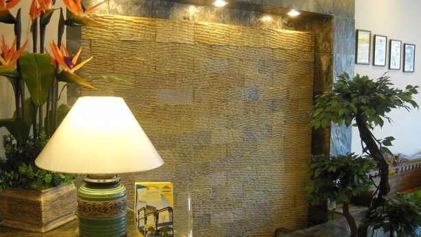 Una zona de recepción con pared texturizada, una lámpara de pie y plantas en macetas.