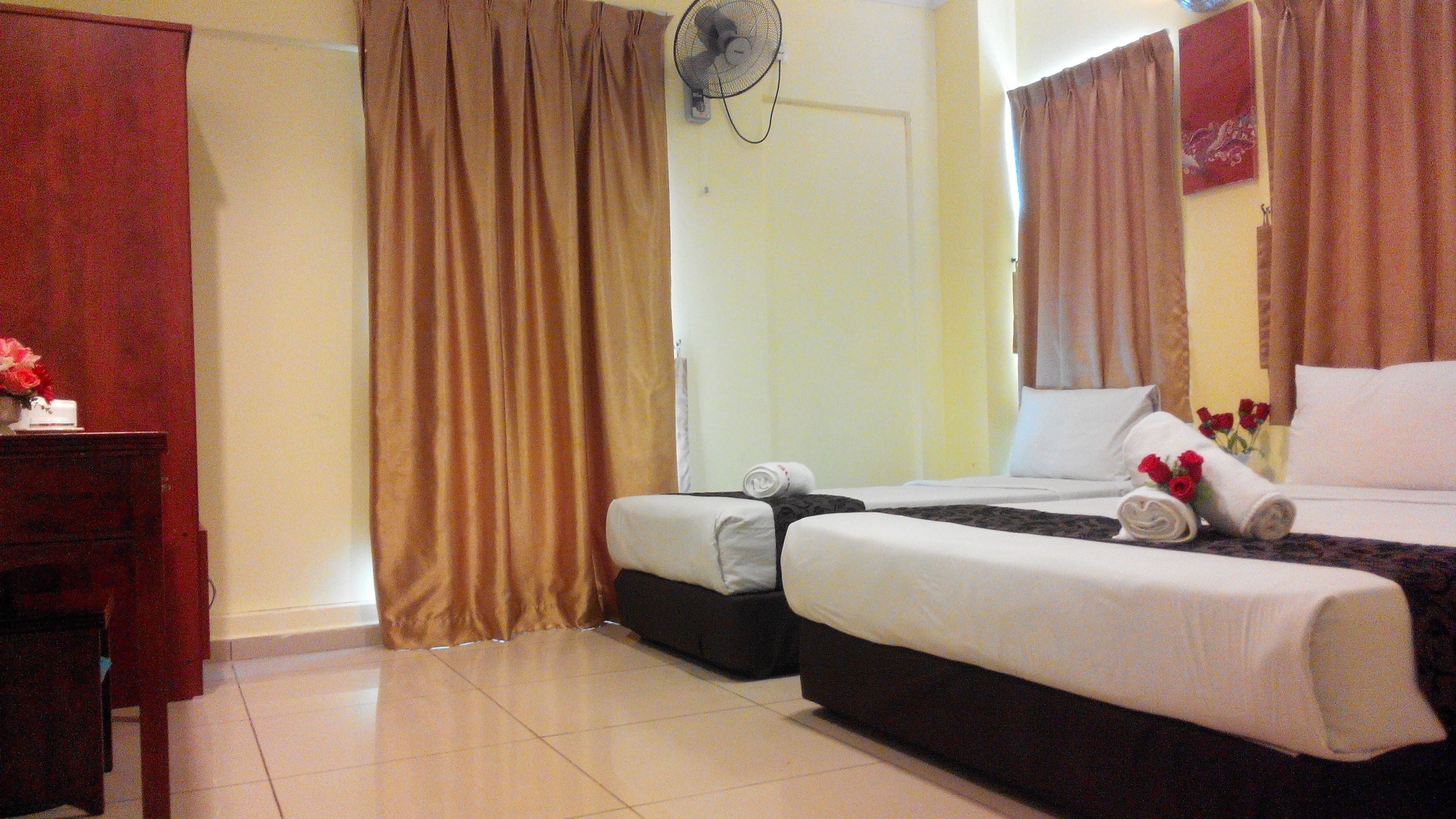 A hotel room with two beds, a desk, a fan, and a door.