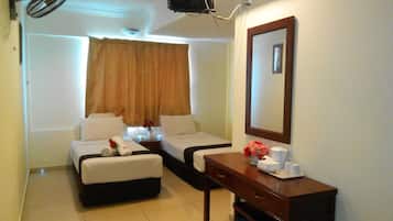 A hotel room with two beds, a desk, a mirror, and a small table with a vase of flowers.