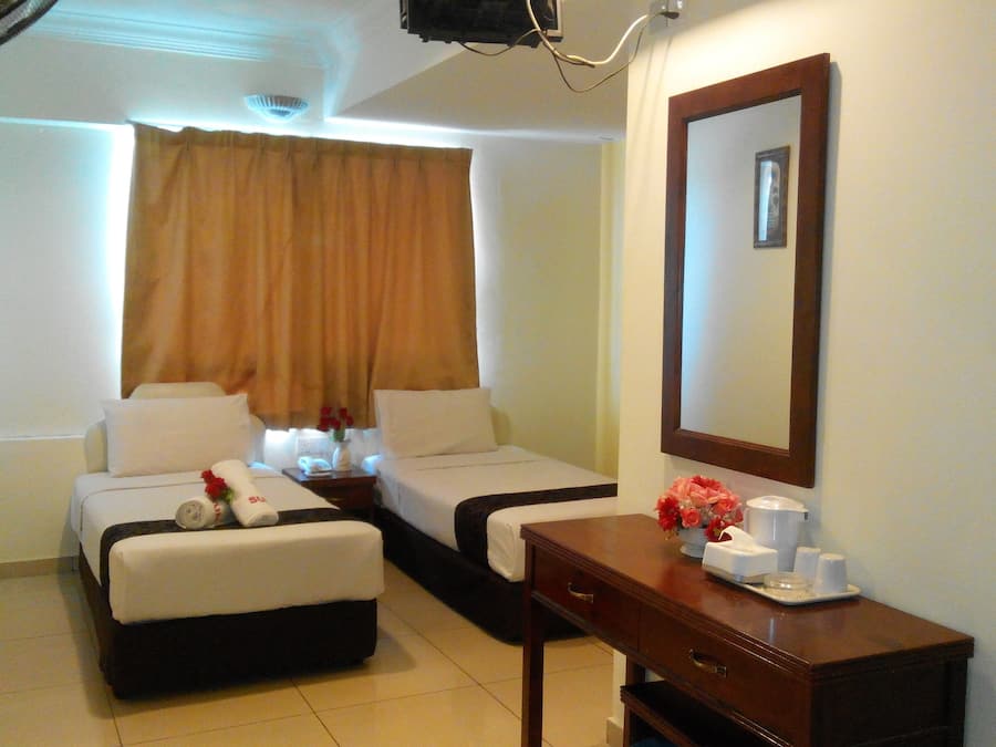 A hotel room with two beds, a desk, a mirror, and a small table with a vase of flowers.