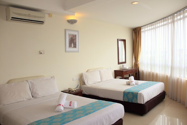 A hotel room with two beds, a nightstand, a desk, a chair, a window with curtains, and a wall-mounted air conditioner.