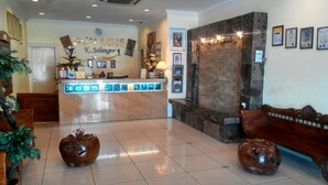 Zona de recepción de hotel con mostrador, cuadros de diplomas y un reloj en la pared.