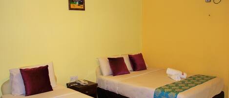 A hotel room with two beds, each with a pillow, a bedside table with a phone, and a wall-mounted fan.