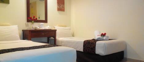A hotel room with two beds, a wooden nightstand with a vase of red flowers, a mirror, and a wall-mounted fan.
