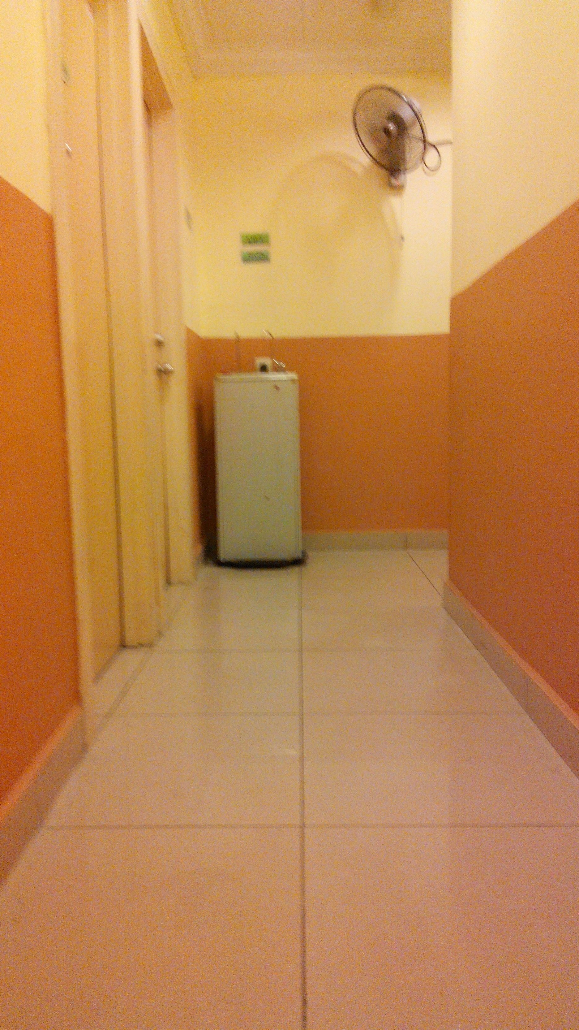 Een smalle gang met een koelkast en een ventilator aan de muur.