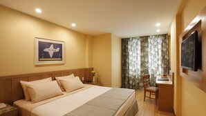 Habitación de hotel con cama, escritorio, silla, televisor y un cuadro en la pared.