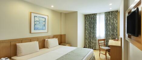 Una habitación de hotel con una cama, un escritorio, un televisor y un cuadro en la pared.