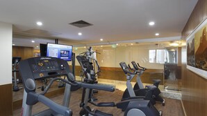 Un gimnasio con máquinas de cardio, una pantalla digital y una pared de vidrio con vistas a la montaña.
