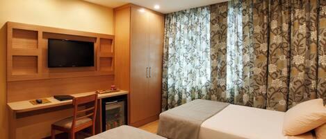 Habitación de hotel con un escritorio de madera, un televisor, dos camas y una cortina estampada con motivos florales.