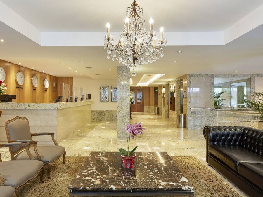 A lobby with a reception desk, a chandelier, a sofa, and a potted orchid.