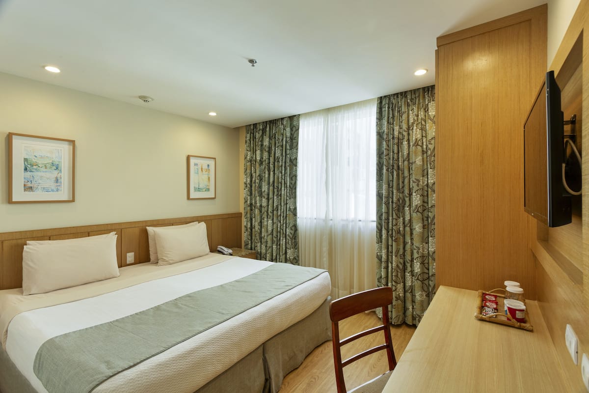 A hotel room with a bed, a desk, a chair, a television, and curtains.