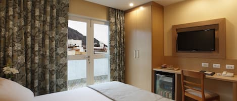 A hotel room with a bed, a desk with a chair, a television, and a minibar.