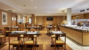 Un restaurante con mesas y sillas de madera, una barra de mármol y un televisor colgado en la pared.