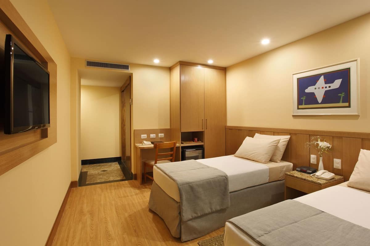 A hotel room with two beds, a desk, a television, a wardrobe, and a painting on the wall.