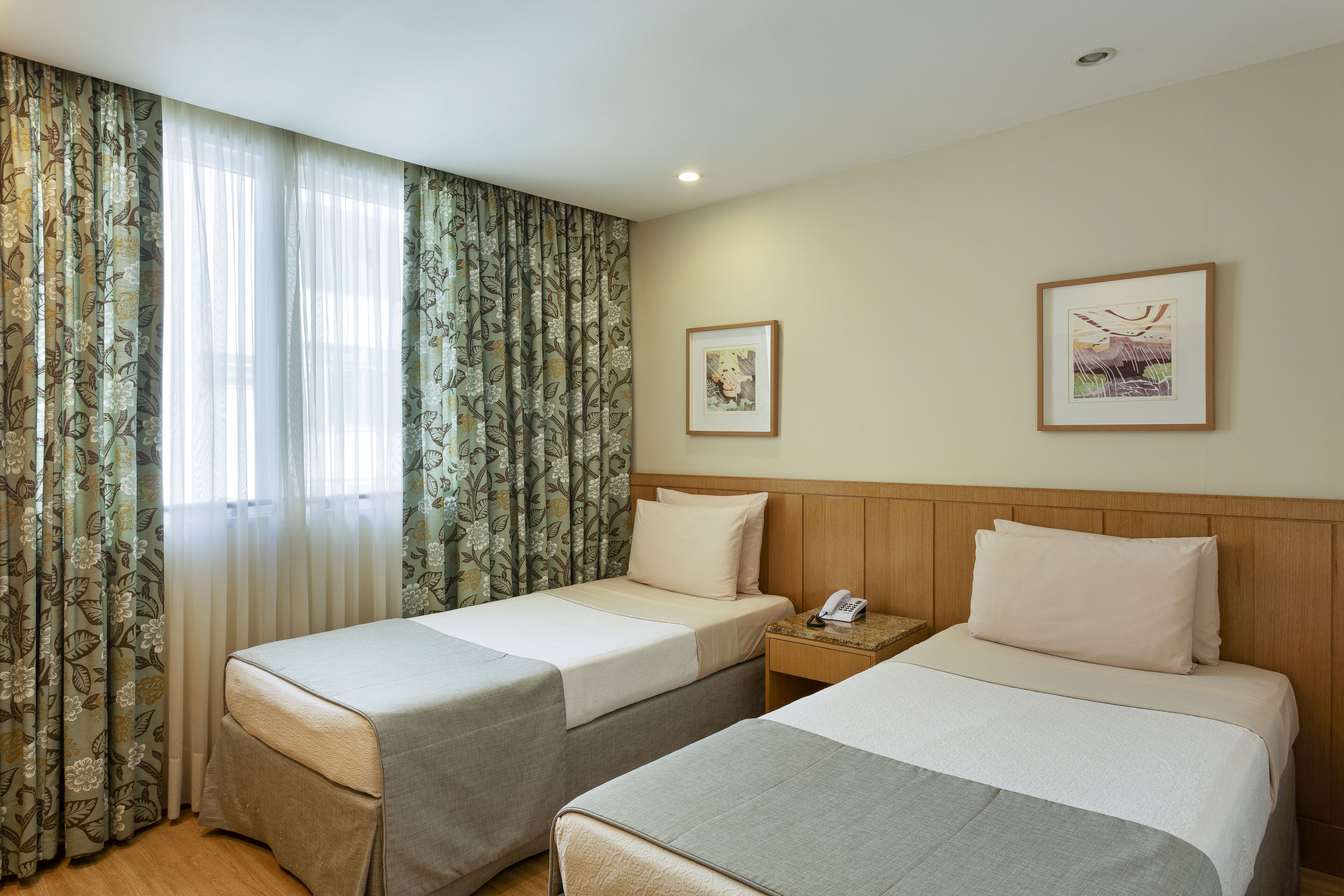 Ein Hotelzimmer mit zwei Betten, einem hölzernen Kopfteil, einem Nachttisch mit Telefon und zwei gerahmten Bildern an der Wand.