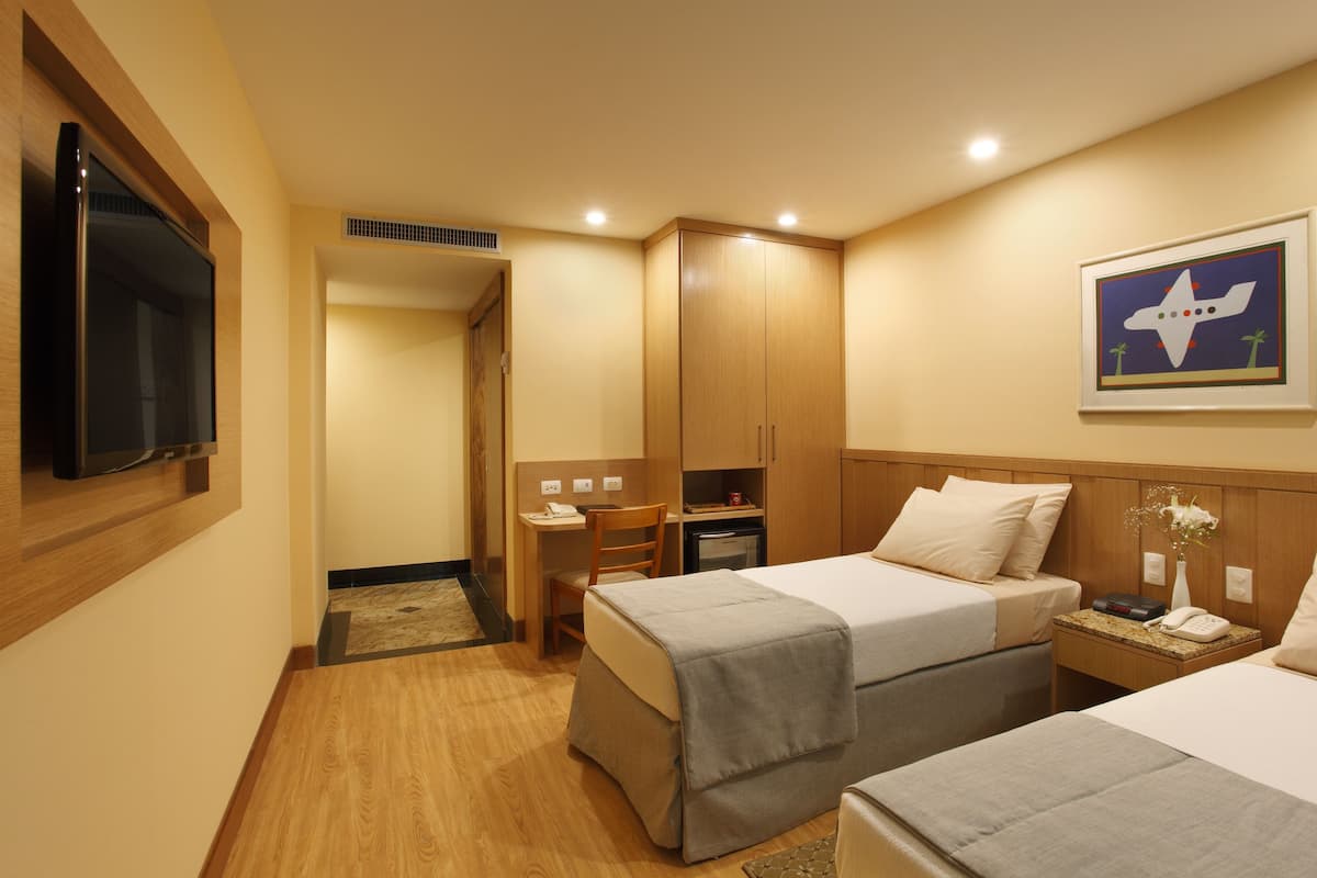 A hotel room with two beds, a desk, a chair, a TV, and a framed picture on the wall.