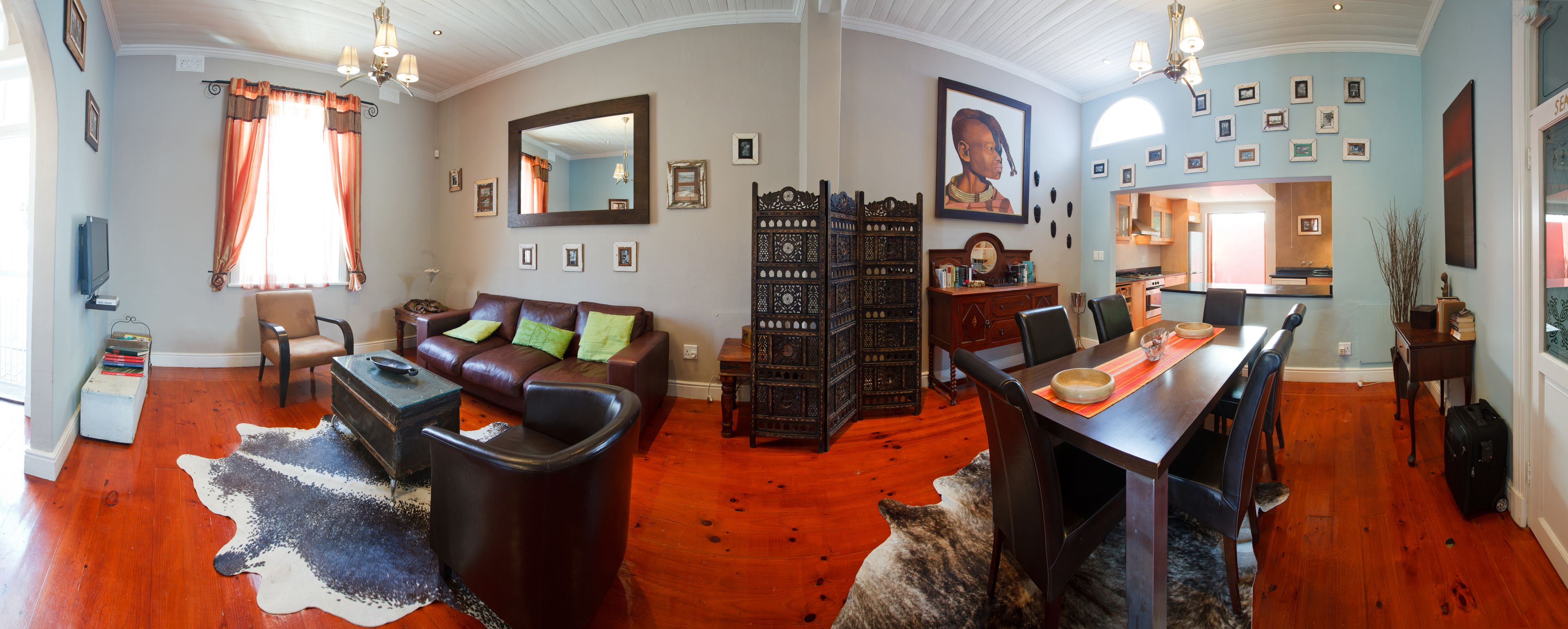 A spacious living room with a leather sofa, a dining table, and a kitchen in the background.