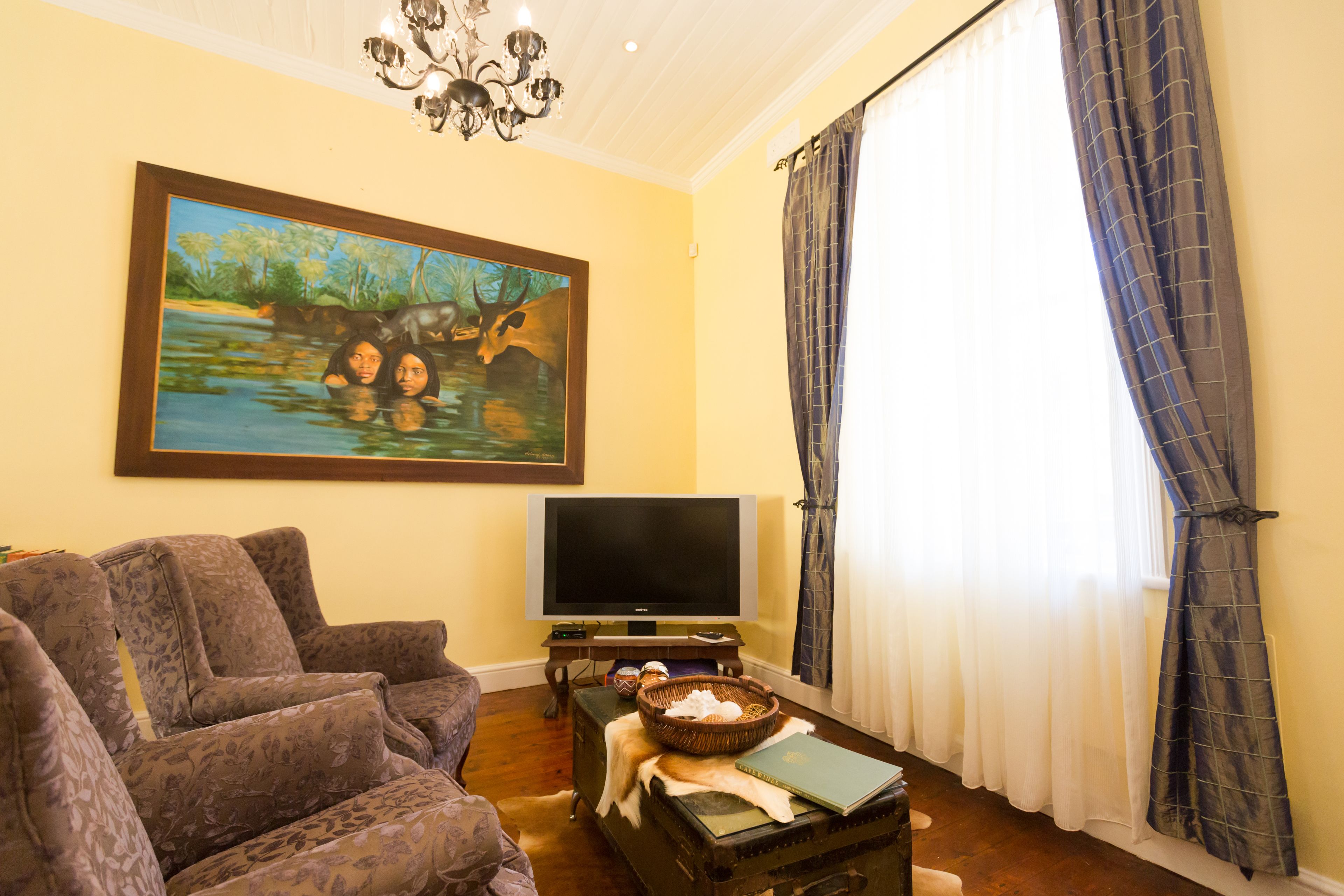 A living room with a sofa, a television, a painting, and a window with curtains.