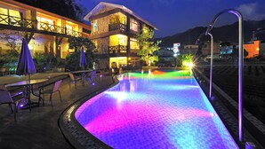 A pool with colorful lighting, outdoor seating, and a building with stone walls and a balcony. - Cimengrou Hall (Dahu)