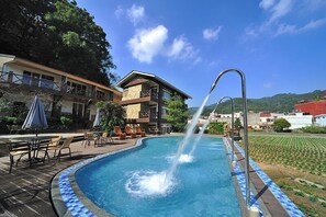 A swimming pool with a water feature, outdoor seating, and a view of the surrounding landscape.