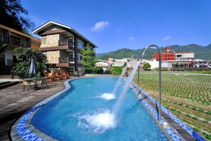 A swimming pool with a water fountain, surrounded by lounge chairs and a wooden deck.