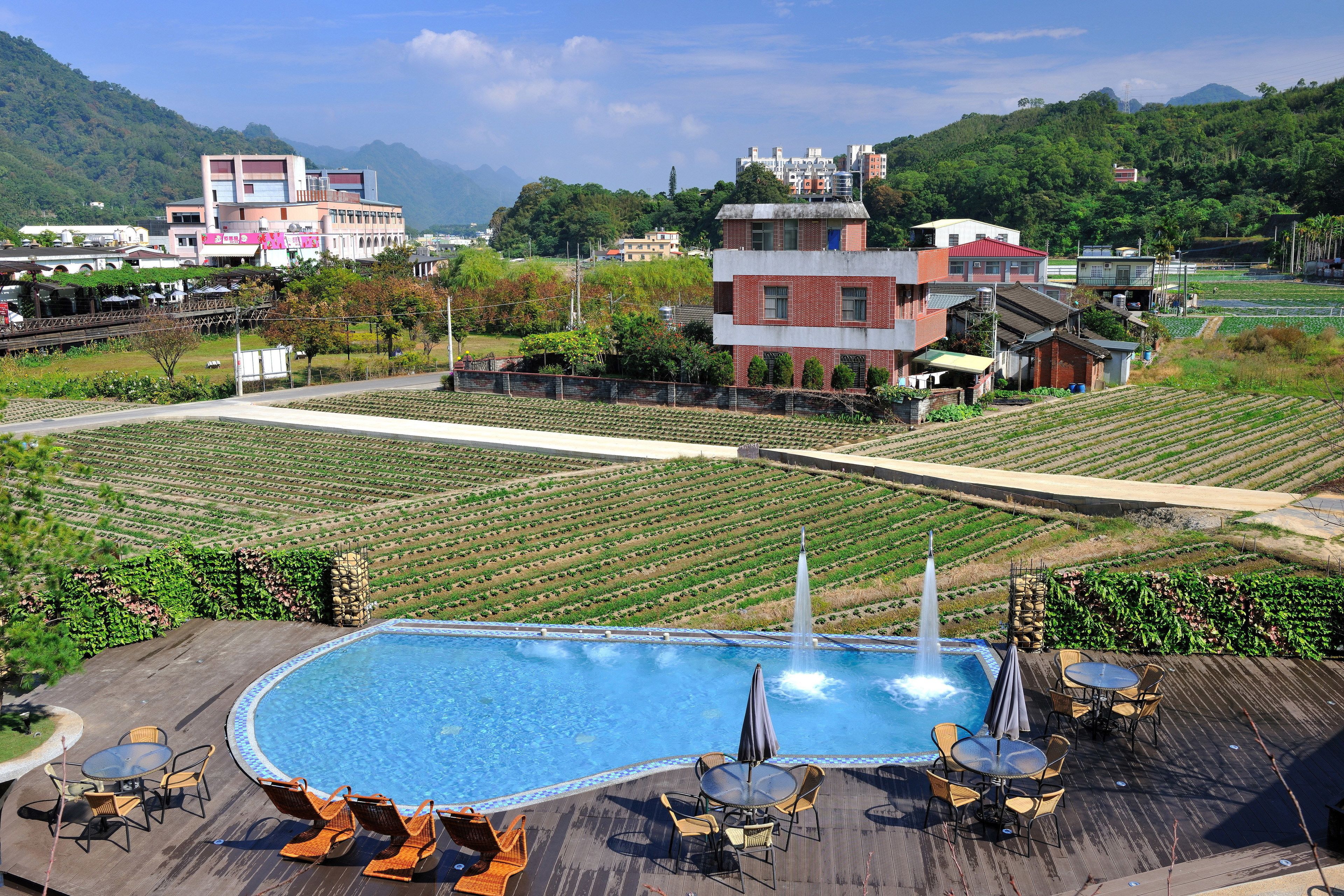 Una piscina con sedie a sdraio e tavoli, circondata da un giardino curato e affacciata su una zona montuosa.
