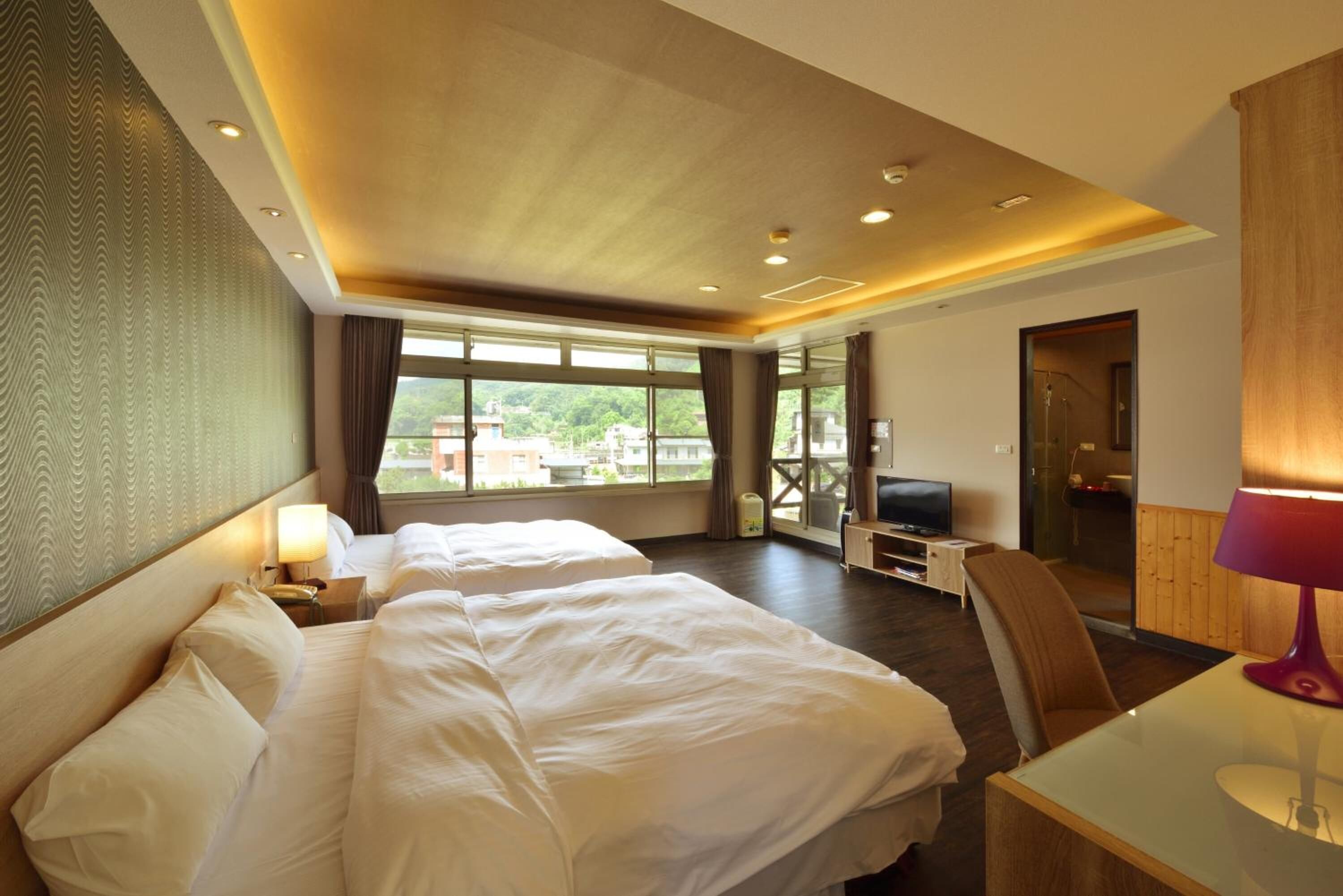 Habitación de hotel con dos camas, televisión, escritorio y vista al exterior.