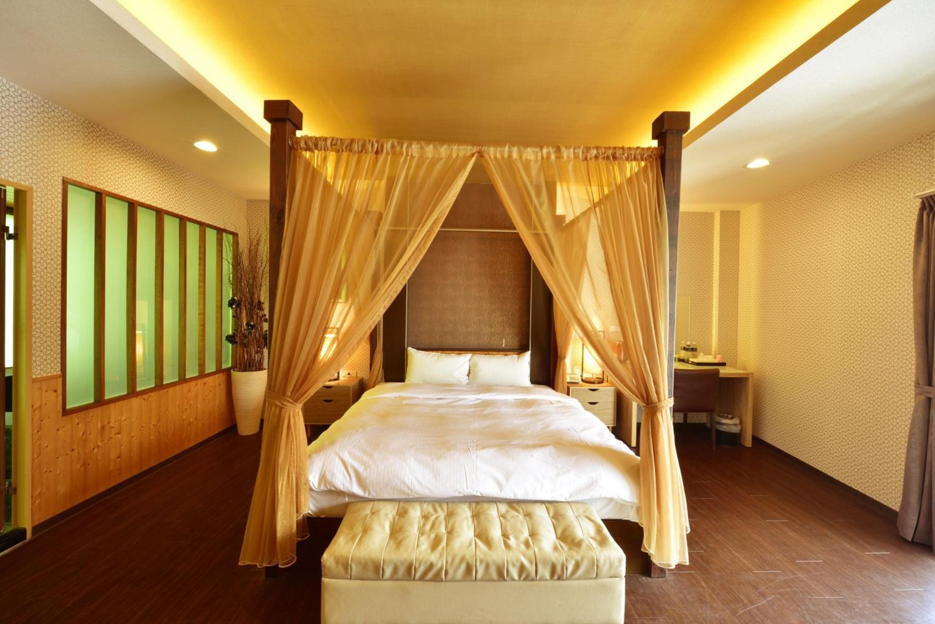 A spacious bedroom with a four-poster bed, a sitting area with a desk, and a large potted plant.