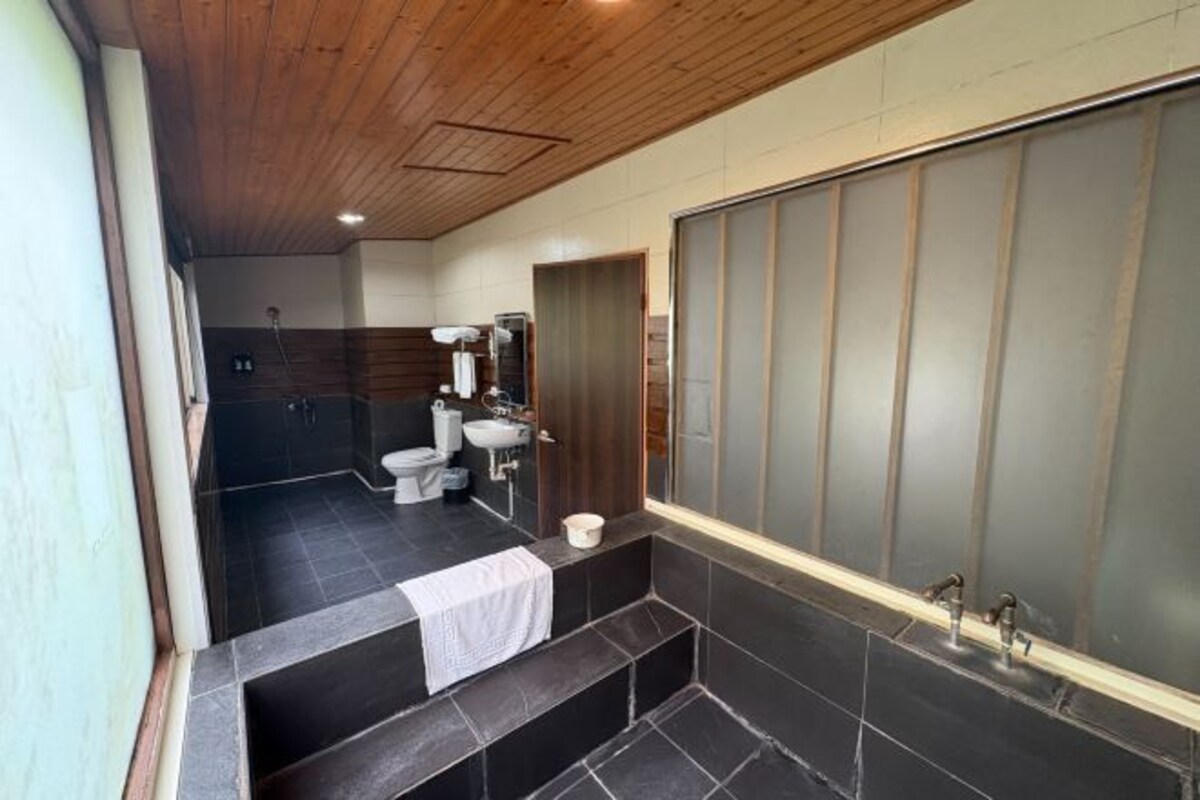 A modern bathroom with a wooden ceiling, a large mirror, a bathtub, and a toilet.