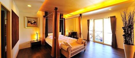 A spacious bedroom with a four-poster bed, a large window with curtains, a potted plant, and a nightstand with a lamp.