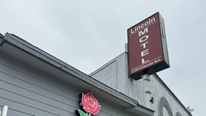 Exterior do Motel Lincoln, com um letreiro verde chamativo e uma decoração de rosas.