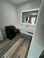 Baño pequeño con lavamanos, espejo y microondas negro.