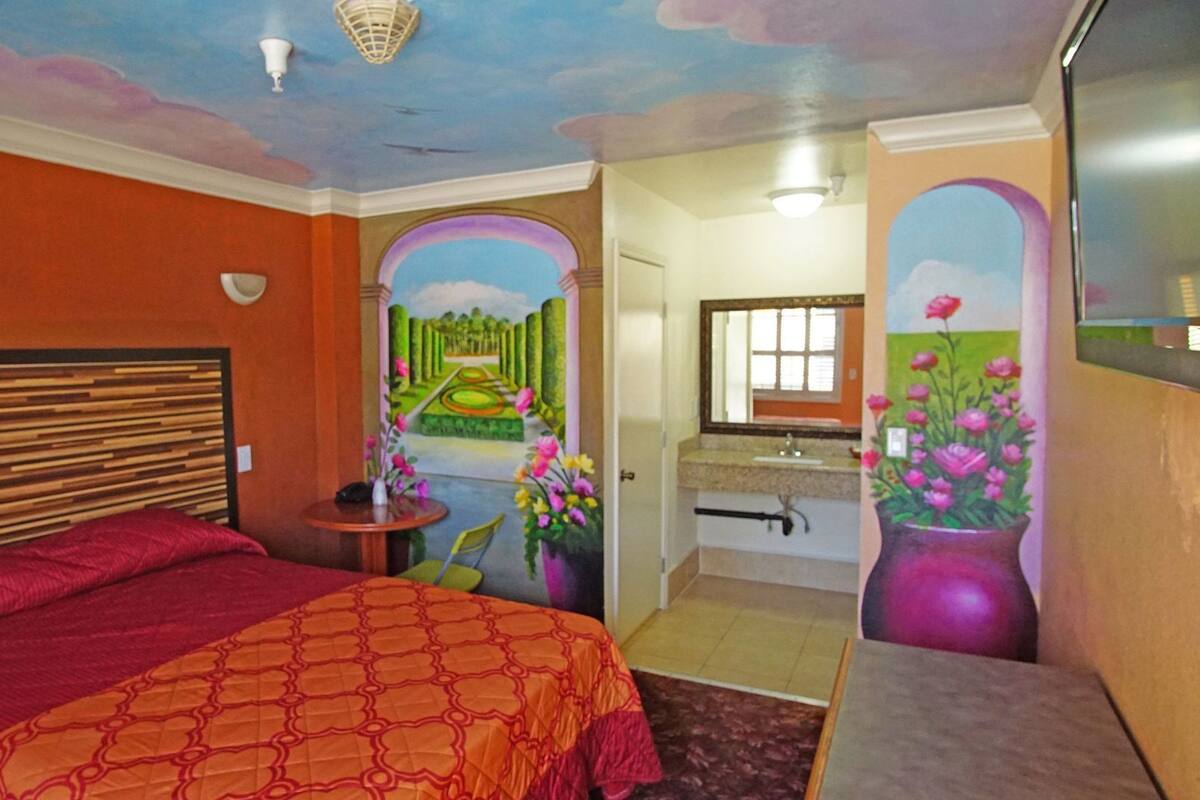 A bedroom with a bed, a nightstand, a mirror, and a bathroom with a sink and toilet.