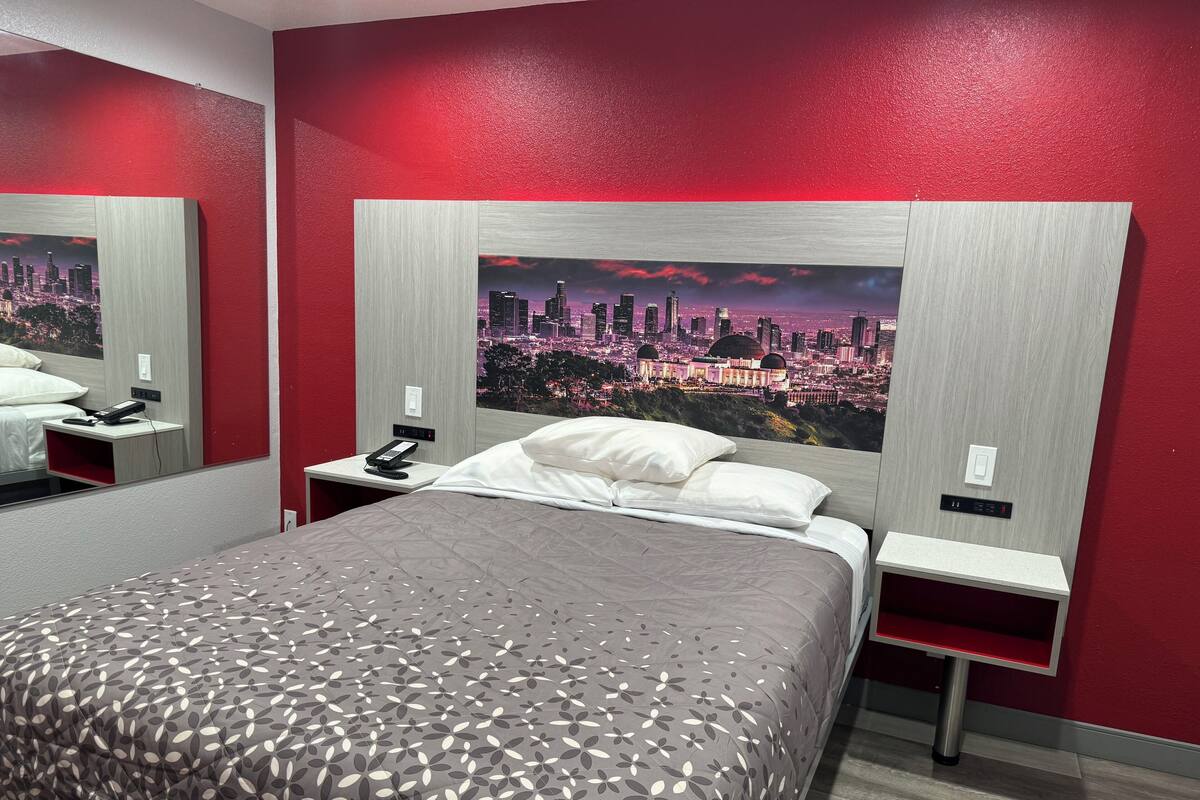 A hotel room with a bed, a nightstand with a phone, a wall-mounted TV, and a cityscape view.