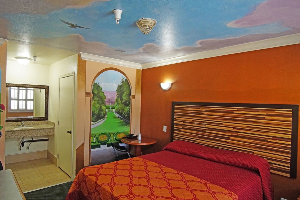Habitación de hotel con cama, baño y vista a un parque a través de un arco.