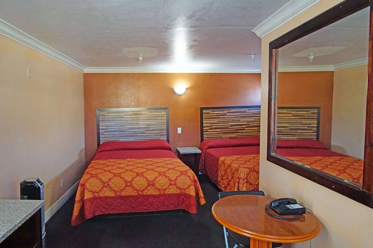 A hotel room with two beds, a small table, a chair, a desk, and a mirror.