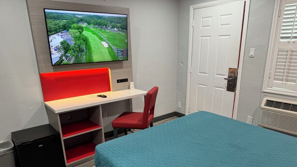 Ein Hotelzimmer mit Bett, Schreibtisch mit rotem Stuhl, Wandfernseher und einer Tür.