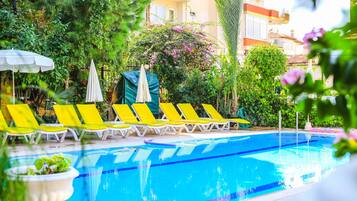 A swimming pool with yellow lounge chairs and umbrellas, surrounded by greenery and a building in the background.