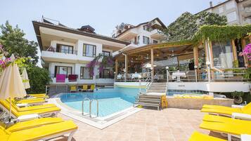 A swimming pool area with yellow lounge chairs, a children's pool, and a covered seating area.