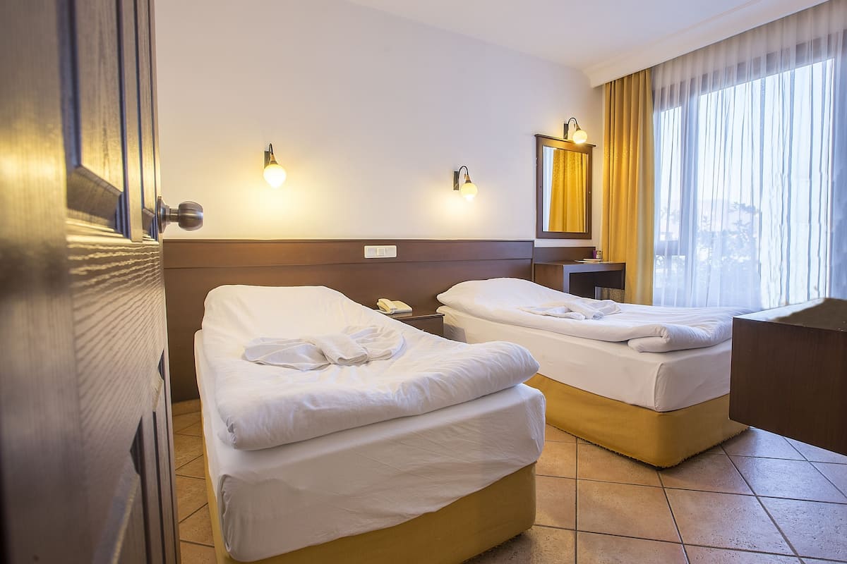 Habitación de hotel con dos camas, una mesita de noche, un espejo y una ventana con cortinas.