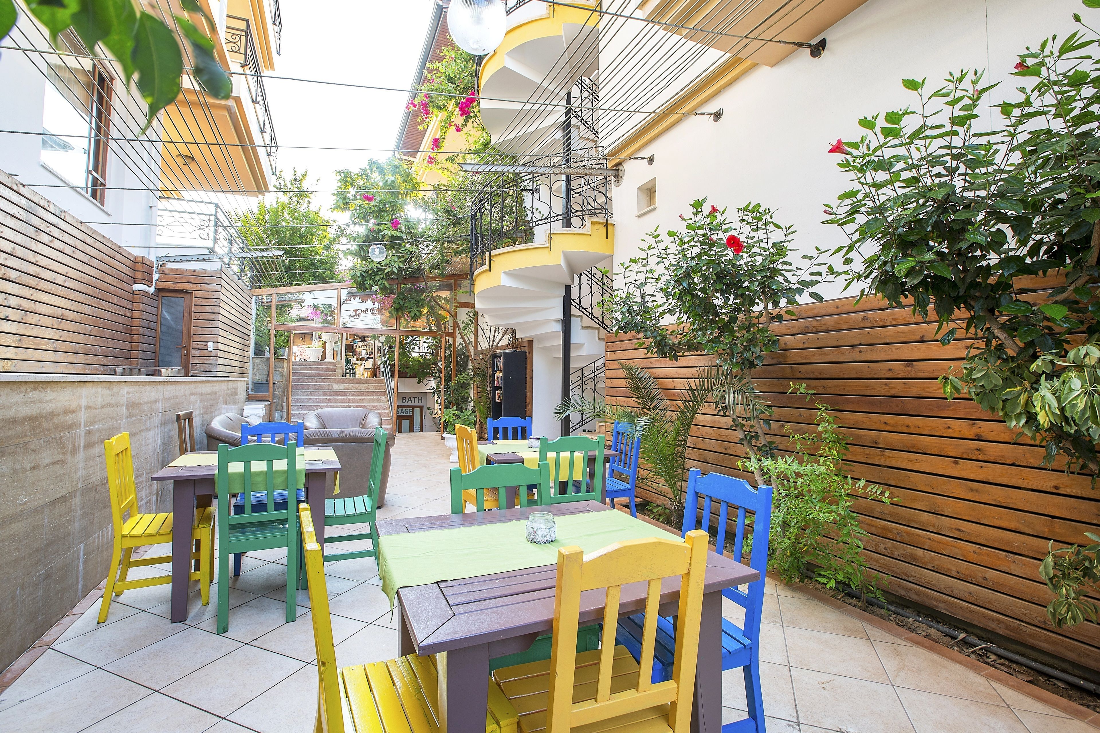 A patio area with outdoor seating, including tables and chairs, surrounded by plants and a wooden fence.